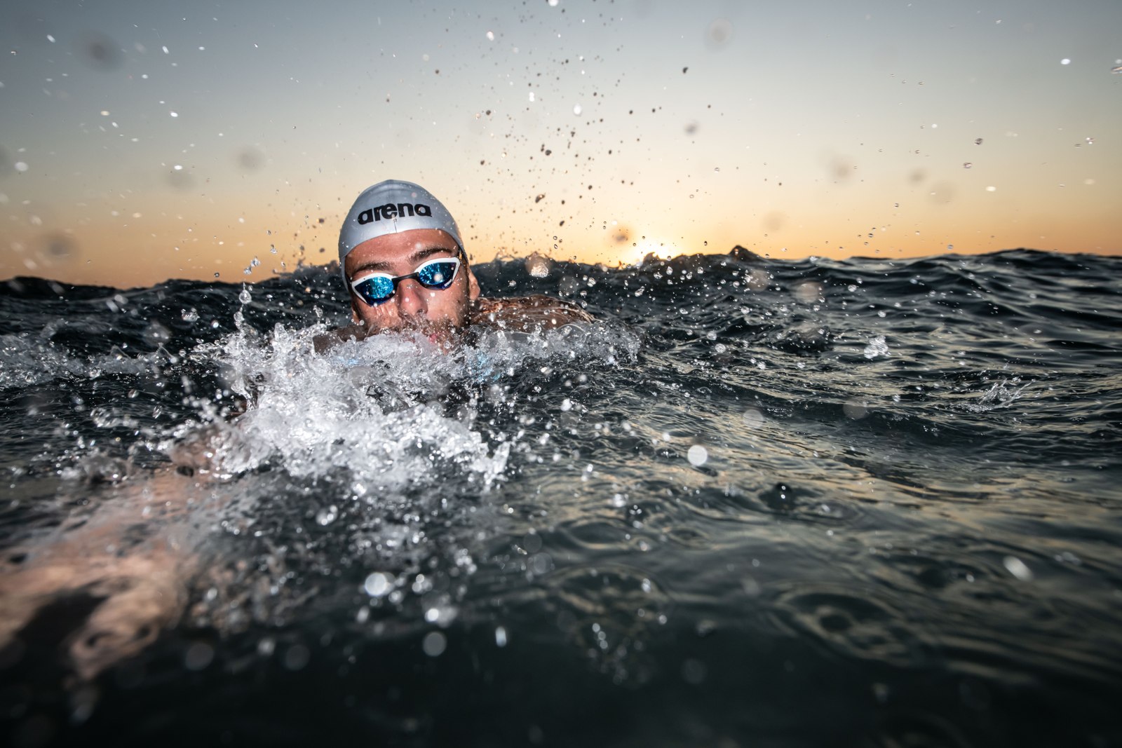Gregorio Paltrinieri swims toward the camera in open water at sunset.