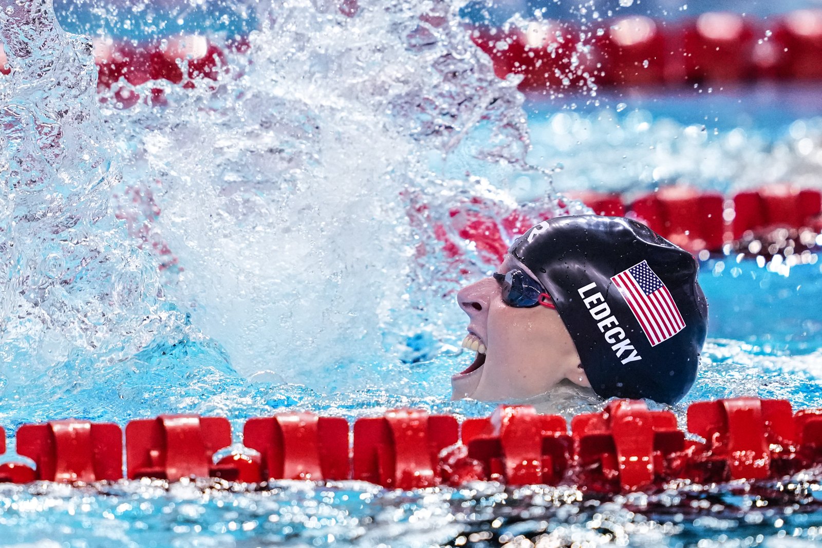 Katie Ledecky races freestyle beside red lane ropes.
