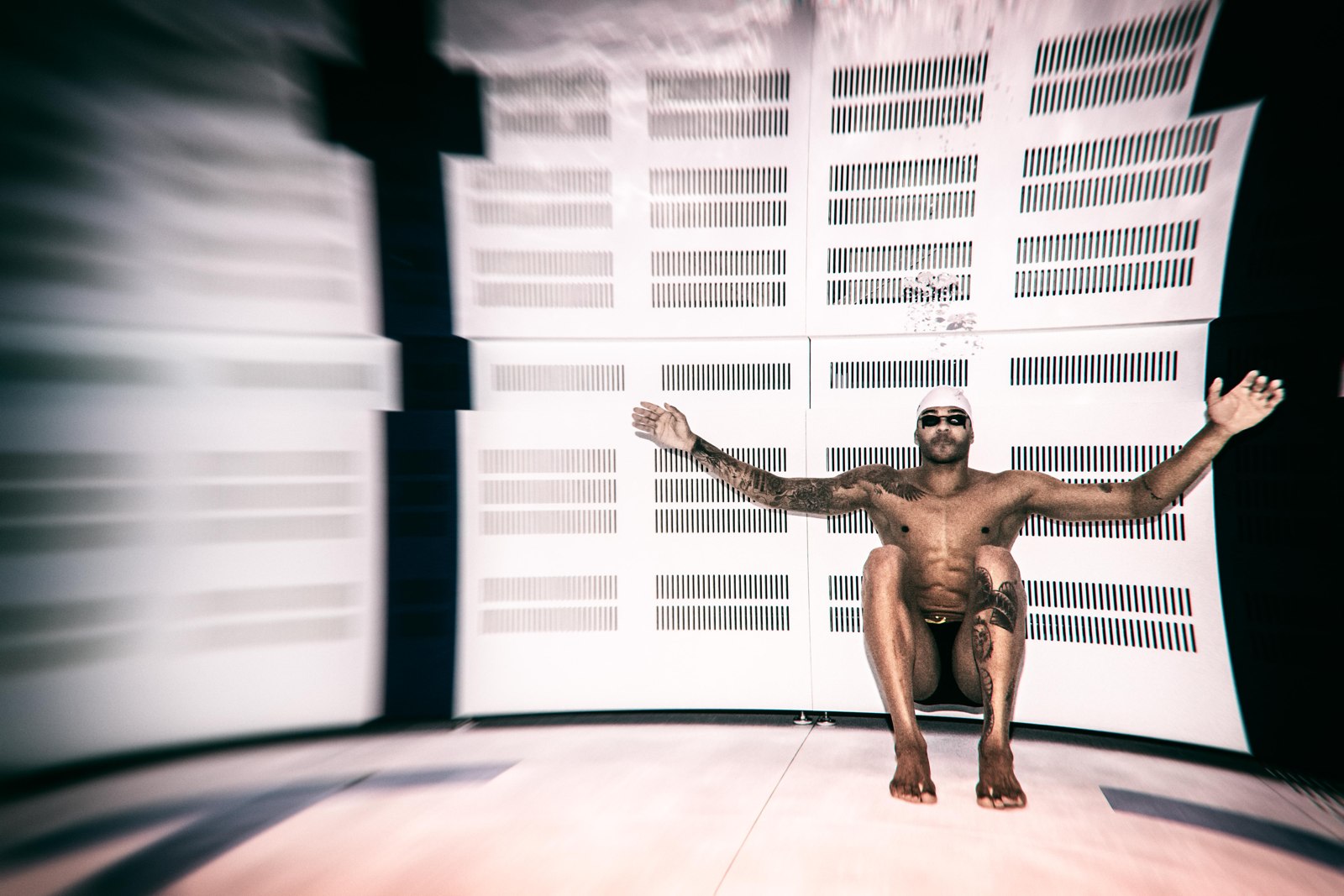 Matheus Santana suspended underwater with his arms outstretched against geometric pool walls.