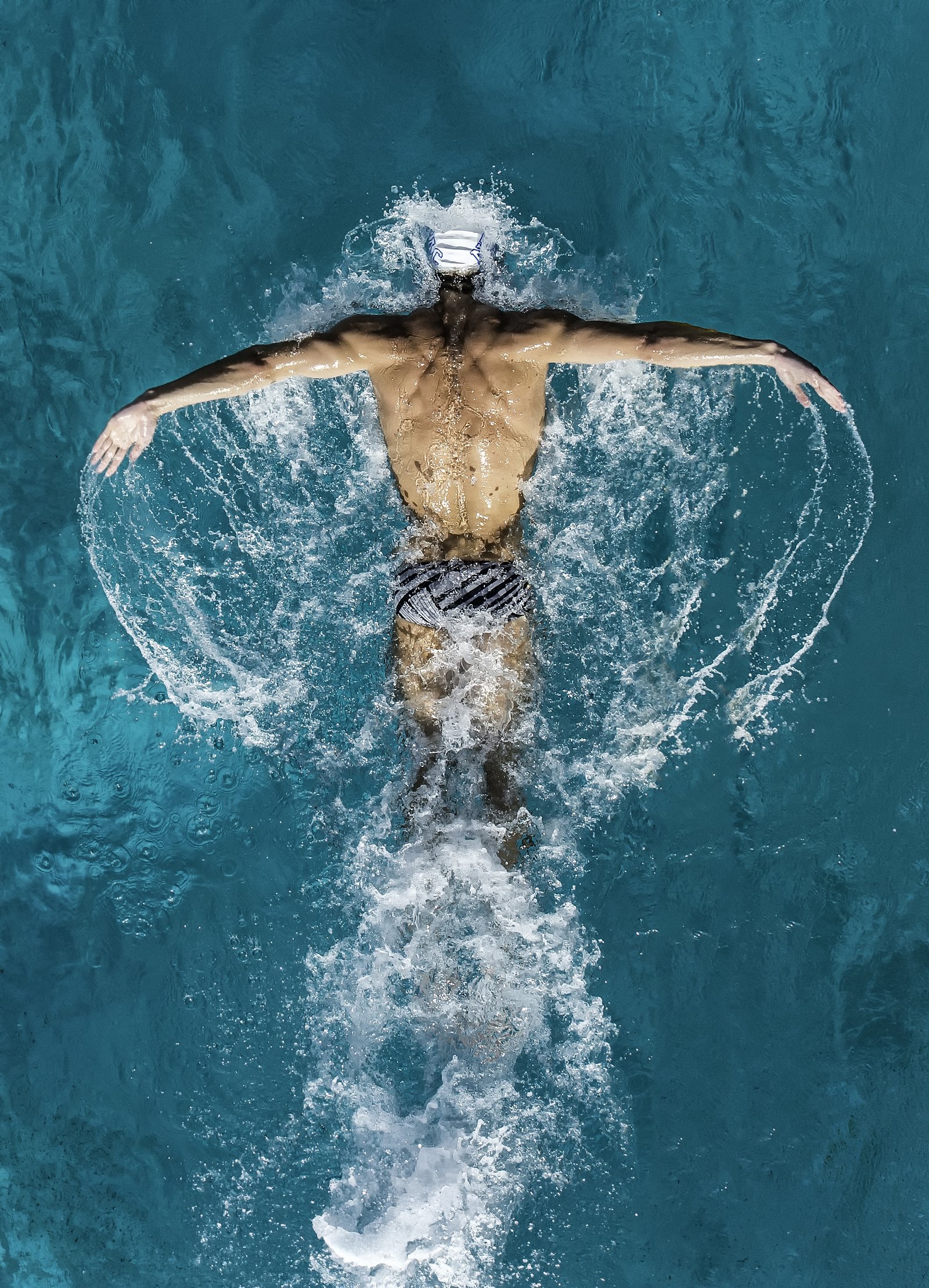 Michael Phelps photographed from above, surrounded by a fan of water.