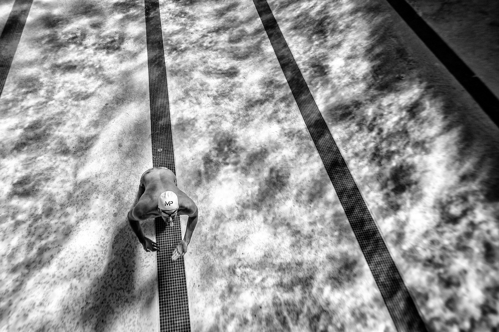 Michael Phelps underwater in black and white, surrounded by patterned light and lane shadows.