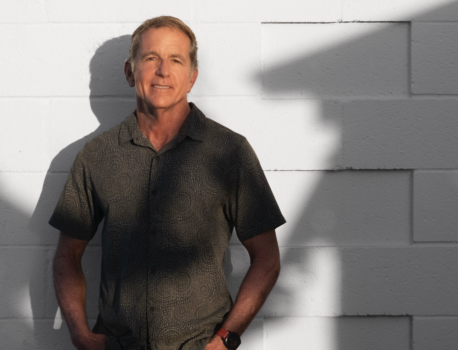 Mike Lewis standing in sunlight beside a white wall.