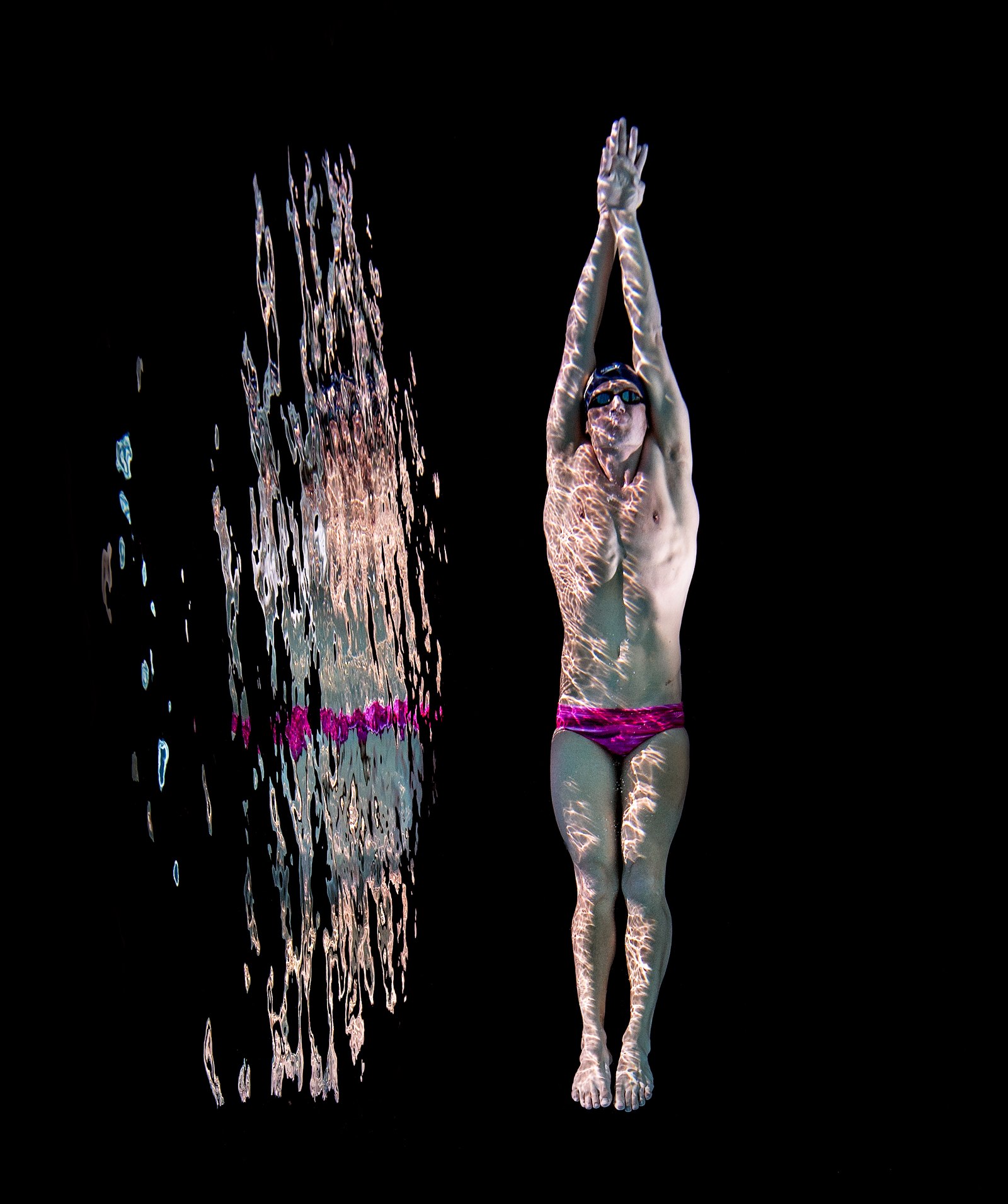 Ryan Lochte holds a streamline position beside his reflection against a black background.